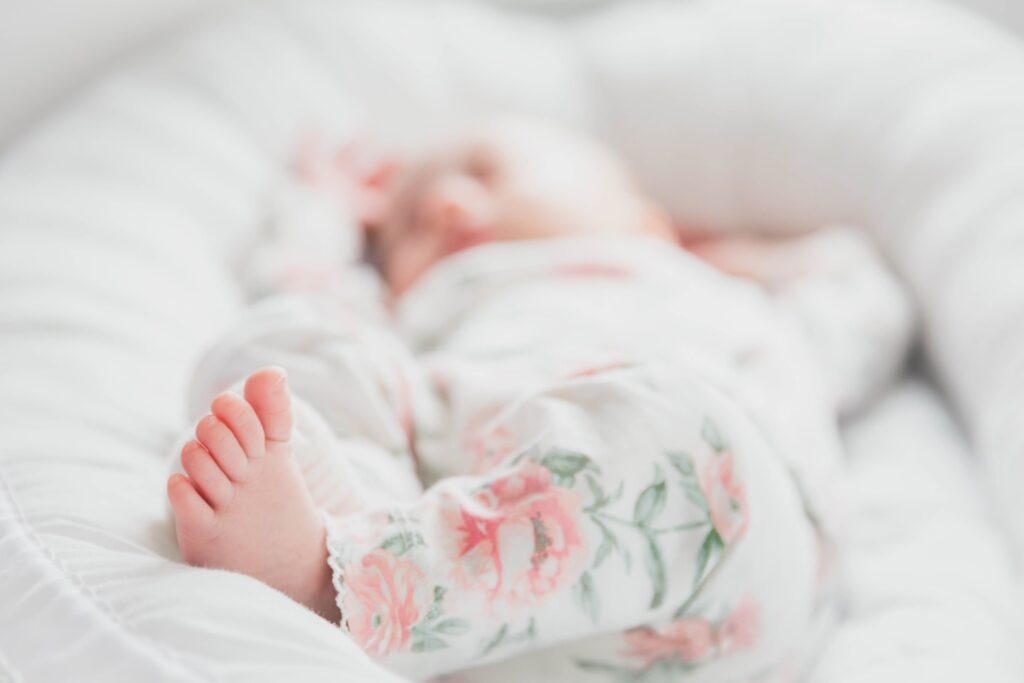 baby in white and red floral onesie lying on bed