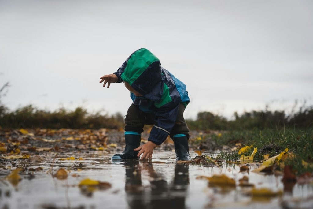 Enfant en veste de pluie et bottes jouant dans une flaque parmi les feuilles d’automne